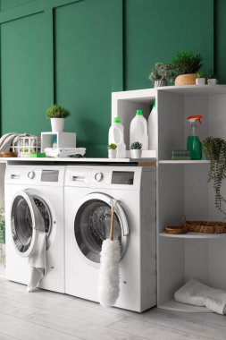 Çamaşır makineleri, raf üniteleri ve yapay bitkilerle dolu bir çamaşırhane.