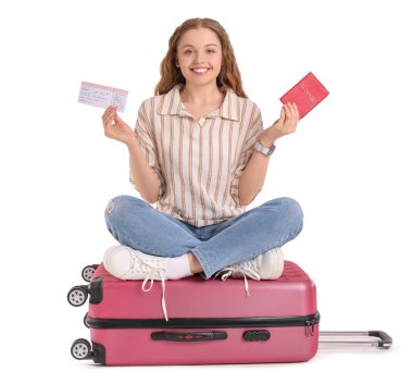 Pasaportu, bileti ve beyaz arka planda valizi olan genç bir kadın.
