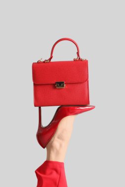 Kırmızı topuklu kadın bacağı, gri arka planda çanta.