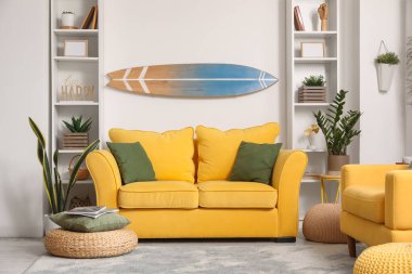 Sörf tahtası, sarı kanepesi ve koltuğu olan bir oturma odası.