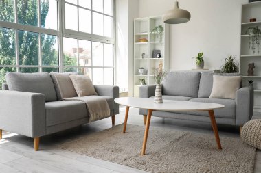 Işıl ışıl oturma odasının içi rahat gri koltuklar, kahve masası ve büyük pencereli.