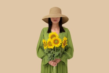 Young woman with beautiful sunflowers on beige background