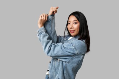 Gri arka planda şık kot elbiseli güzel, mutlu Asyalı kadın.