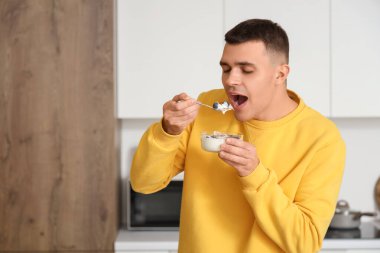 Genç adam mutfakta lezzetli yoğurt yiyor.