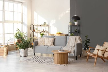 Rahat kanepesi, koltuğu, çiçekleri, raf üniteleri ve masası olan modern oturma odasının güzel iç mekanı.