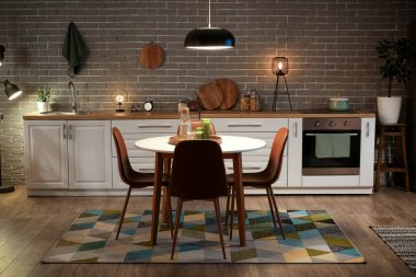 Parlayan lambalar, beyaz tezgahlar, fırın ve akşam yemeği masası olan mutfağın içi.