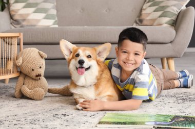 Little happy Asian boy reading book with cute Corgi dog at home