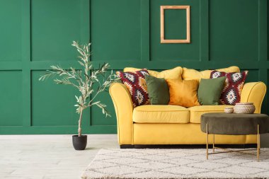 Şık oturma odasının içinde sarı kanepe, sehpa ve zeytin ağacı.