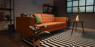 Sıcak kanepe, sehpa ve modern oturma odasının içinde parlayan lambalar.