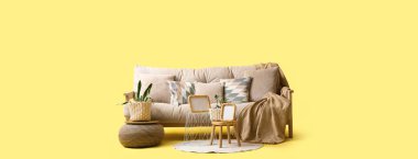 Rahat kanepe, ev bitkileri, masalar ve sarı arka planda puf.