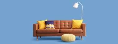 Mavi arka planda rahat bir kanepe, lamba ve puf.