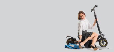 Elektrikli scooter 'ı olan yorgun genç bir iş kadını. Gri arka planda ayakkabılarını çıkarıyor. Mesaj için yeri var.