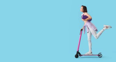 Mavi arka planda scooter süren genç ve sportif bir kadın.