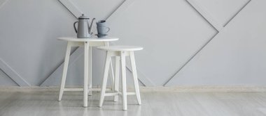 Gri duvarın yanında çaydanlık ve fincanlarla süslü masalar.