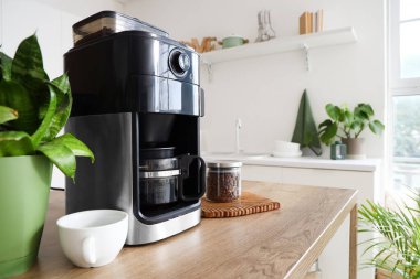 Mutfaktaki ahşap masada bir kavanoz fasulye ve fincanla modern kahve makinesi.