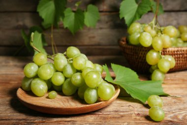 Tabak ve hasır kâse, ahşap arka planda tatlı yeşil üzümler.