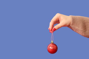 Kırmızı manikürlü bir kadın ve mavi arka planda bir Noel topu.