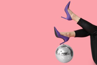 Pembe arka planda disko topu olan şık topuklu kadın bacakları.