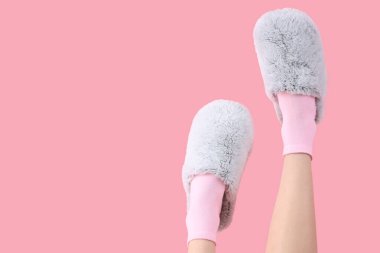 Pembe arka planda gri yumuşak terlikler giyen kadın bacakları.
