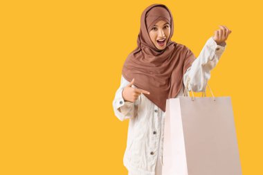Sarı arka plandaki alışveriş çantalarını gösteren güzel Müslüman kadın.