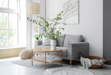 Oturma odasındaki sehpanın üzerinde çiçek açan bir vazo ve rahat bir kanepe.