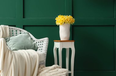 Masasında nergis olan vazo ve oturma odasındaki yeşil duvarın yanındaki koltuk.