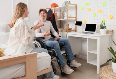 Tekerlekli sandalyedeki erkek mezun evde arkadaşıyla konuşuyor.