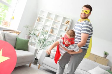 Süper kahraman kostümlü babasıyla evde eğlenen küçük bir çocuk.