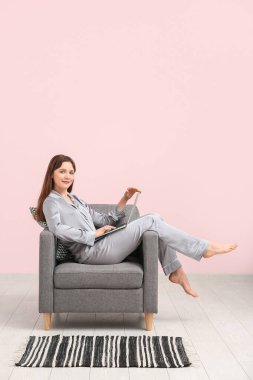 Pijamalı genç bir kadın evdeki siyah koltukta dizüstü bilgisayarla çalışıyor. Uzak çalışma konsepti