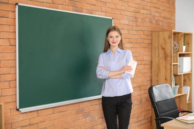 Sınıfta temiz yazı tahtasının yanında bez parçası olan kadın öğretmen.