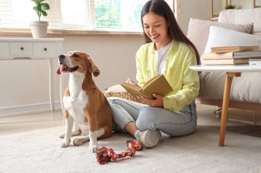 Oturma odasında yerde sevimli bir tazı köpeğiyle kitap okuyan genç bir kadın.