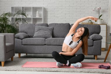 Güzel genç bir kadın oturma odasında yoga yapıyor.