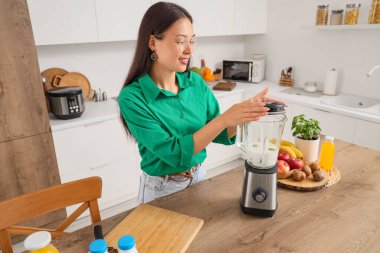 Genç Asyalı kadın mutfakta blender ile smoothie yapıyor.