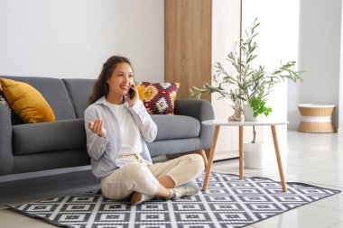 Evde cep telefonuyla konuşan genç Asyalı kadın.