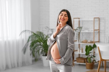 Evde yüz masajı aleti kullanan güzel hamile bir kadın.