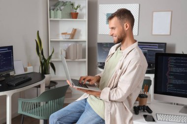 Masada dizüstü bilgisayarla çalışan genç sakallı programcı.