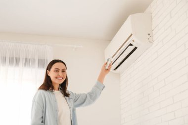 Evinde klima uzaktan kumandası kullanan güzel bir genç kadın.