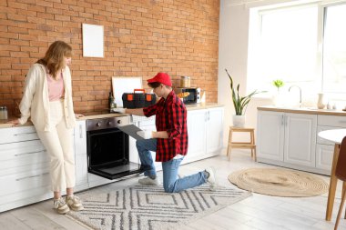 Erkek teknisyen mutfakta kadının fırınını kontrol ediyor.