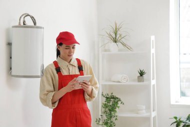 Tuvaletteki modern elektrikli kazanın yanında tablet bilgisayarı olan kadın işçi.