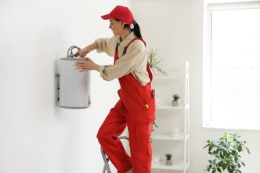 İngiliz anahtarı olan kadın işçi banyoya modern elektrikli kazan kuruyor.