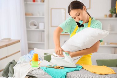 Evde telefonla konuşurken bebek ütüsü yapan Asyalı bir anne. Çoklu görev kavramı