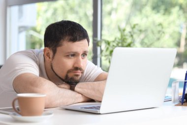 Evde bilgisayar ve bir fincan kahveyle ders veren yorgun genç erkek öğretmen.