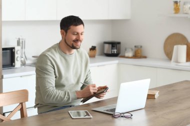 Dizüstü bilgisayarı ve not defteri olan genç erkek öğretmen evde online ders veriyor.
