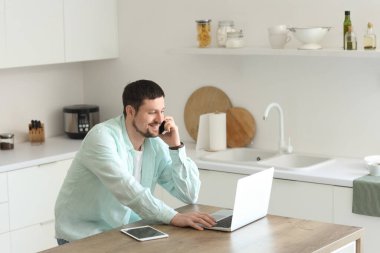 Bilgisayarlı ve cep telefonlu genç erkek öğretmen evde online ders veriyor.