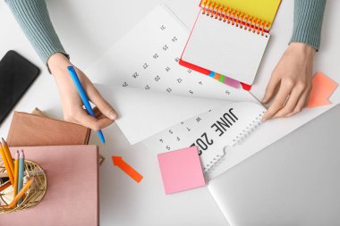 Takvim ve dizüstü bilgisayarı olan genç bir kadın ofiste planlar yapıyor.