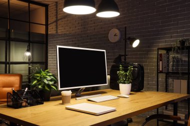 Çalışma odası boş bilgisayar, bitkiler ve karanlık ofiste parlayan lambalar.