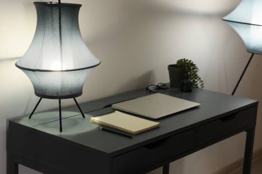 Geceleri ofiste gri duvarın yanında lamba ve modern dizüstü bilgisayarı olan şık bir iş yeri.