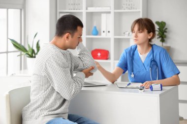 Dirseğinde ağrısı olan genç bir adam hastanede ziyaretçi doktor.