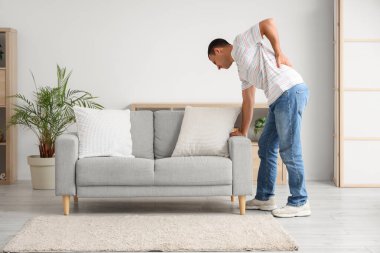 Evdeki kanepenin yanında sırt ağrısı çeken genç bir adam.