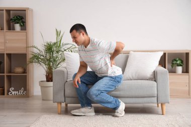 Evdeki kanepenin yanında sırt ağrısı çeken genç bir adam.